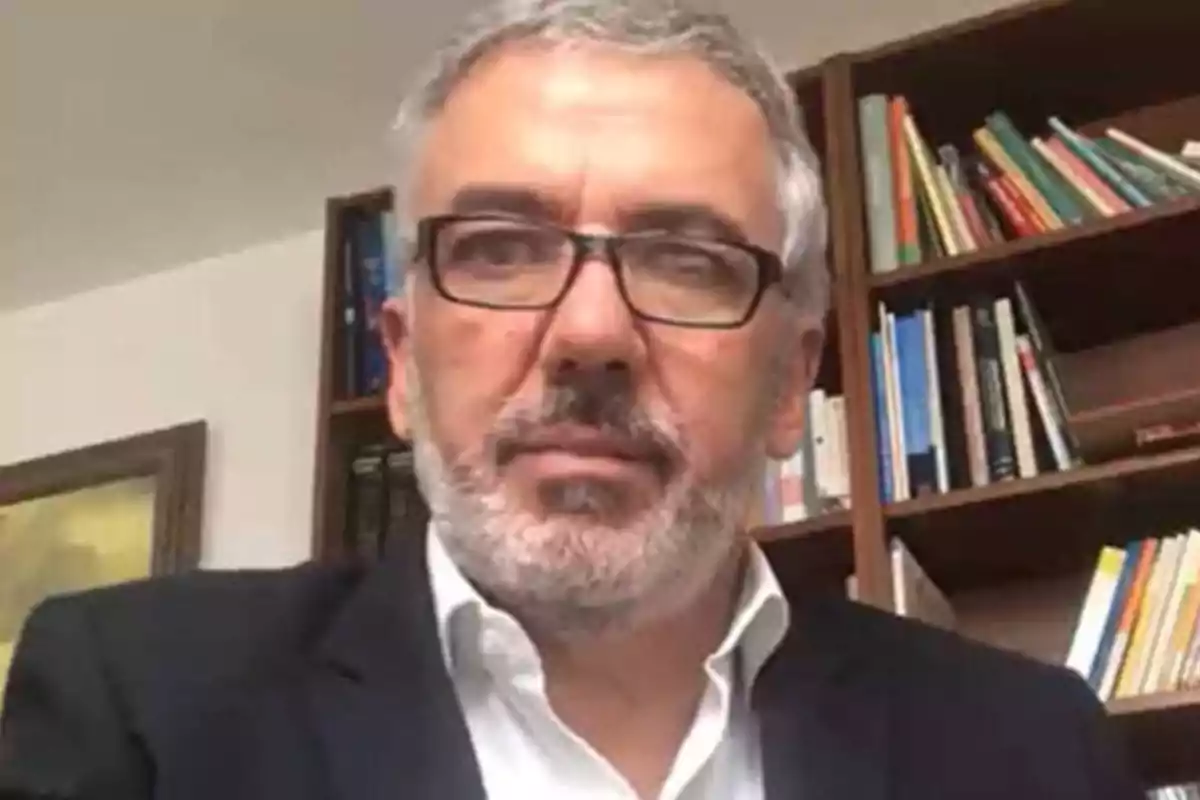 Hombre con gafas y barba gris frente a una estantería con libros.