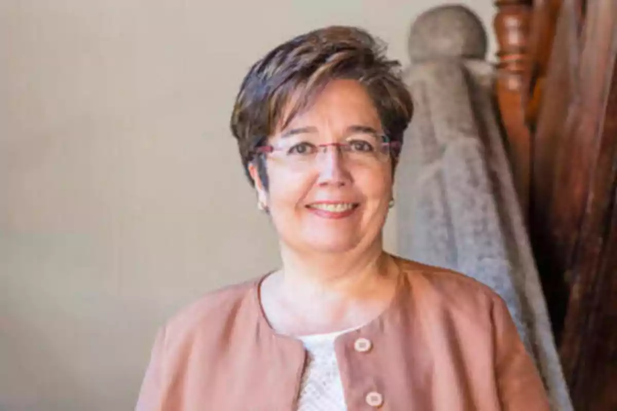 Mujer con gafas y cabello corto sonríe mientras está de pie frente a una barandilla de madera.