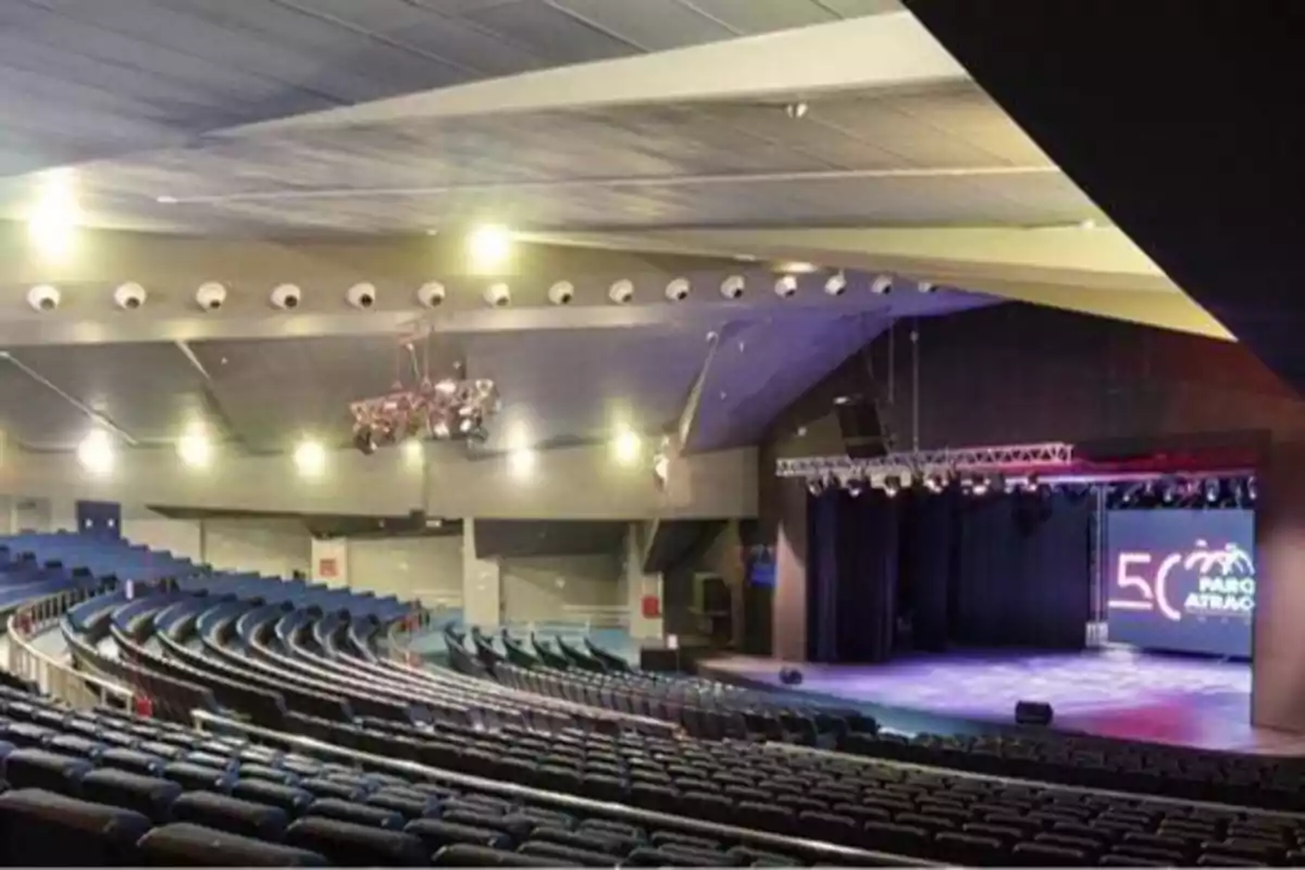 Auditorio vacío con asientos azules y un escenario iluminado al fondo.