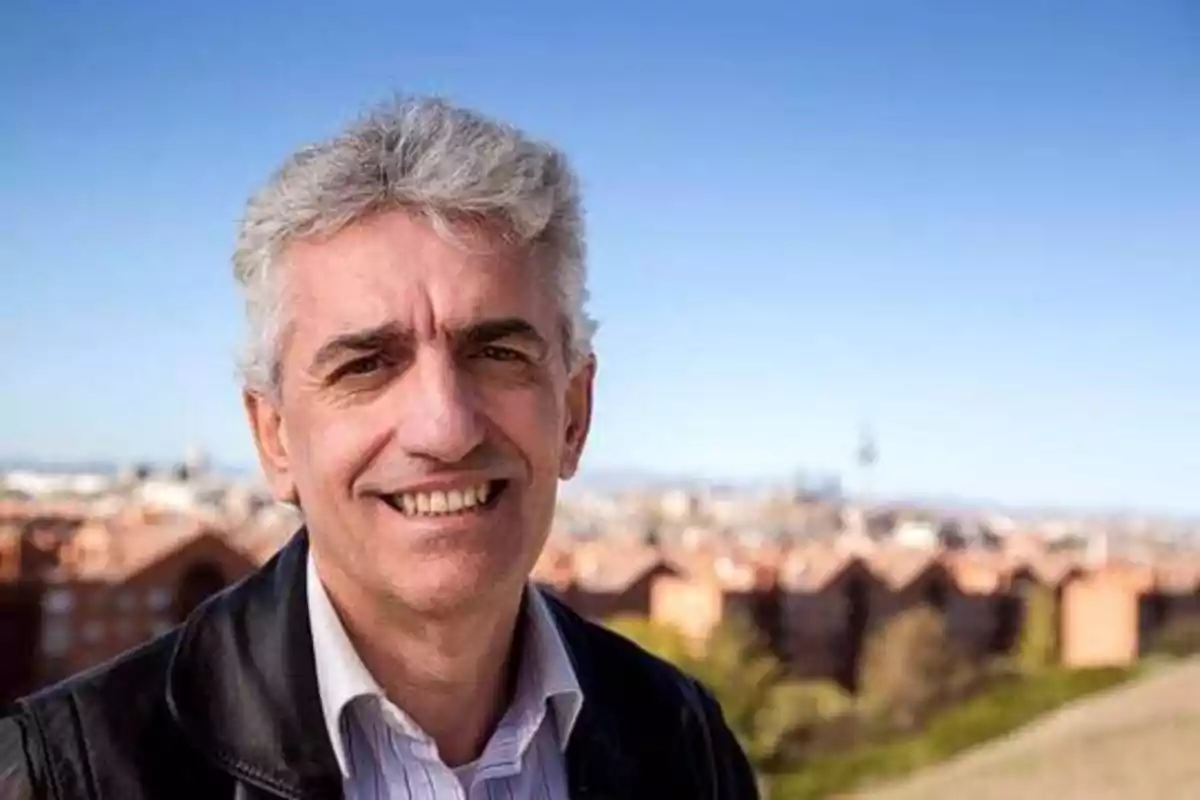 Hombre de cabello canoso sonriendo con una ciudad de fondo.