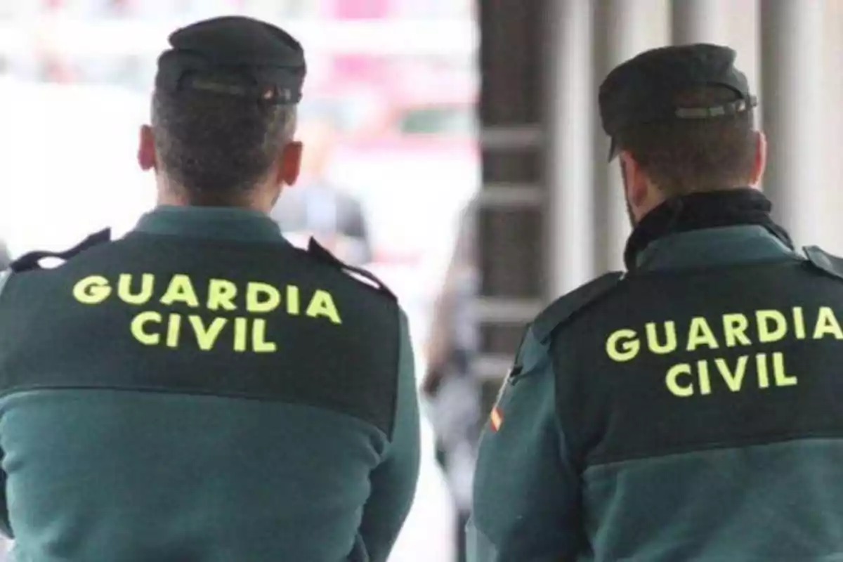 Dos agentes de la Guardia Civil de espaldas con uniformes verdes y letras amarillas.