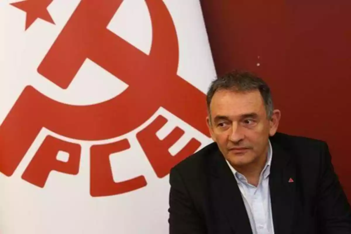 Hombre sentado frente a un logotipo del Partido Comunista de España (PCE) en una pared roja.