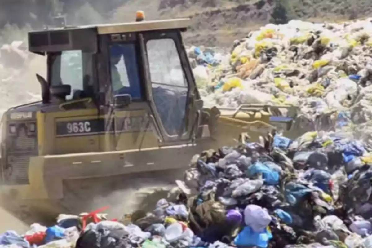 Una excavadora moviendo una gran cantidad de basura en un vertedero.