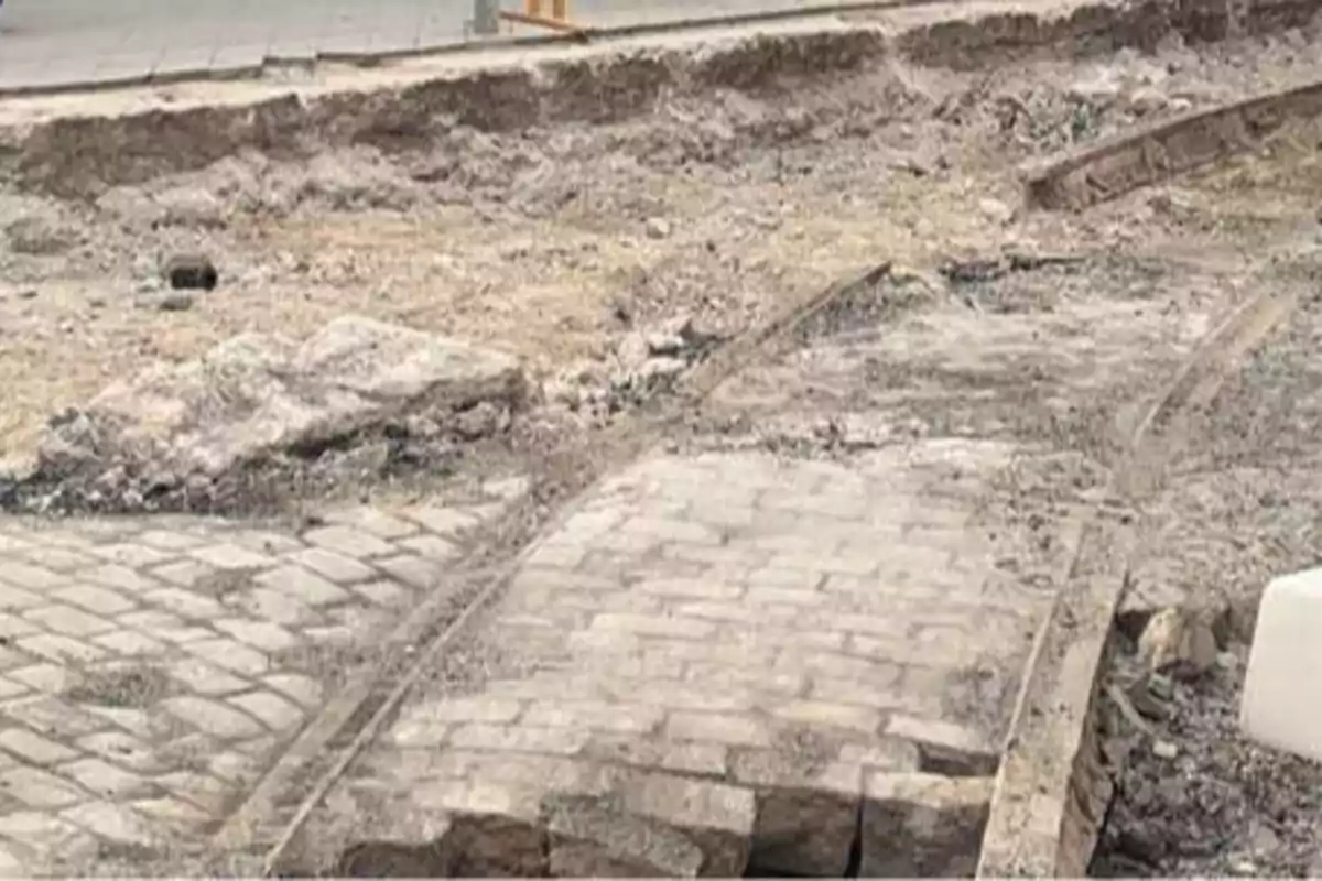 La imagen muestra una sección de una calle en construcción, con adoquines parcialmente removidos y rieles de tranvía expuestos.