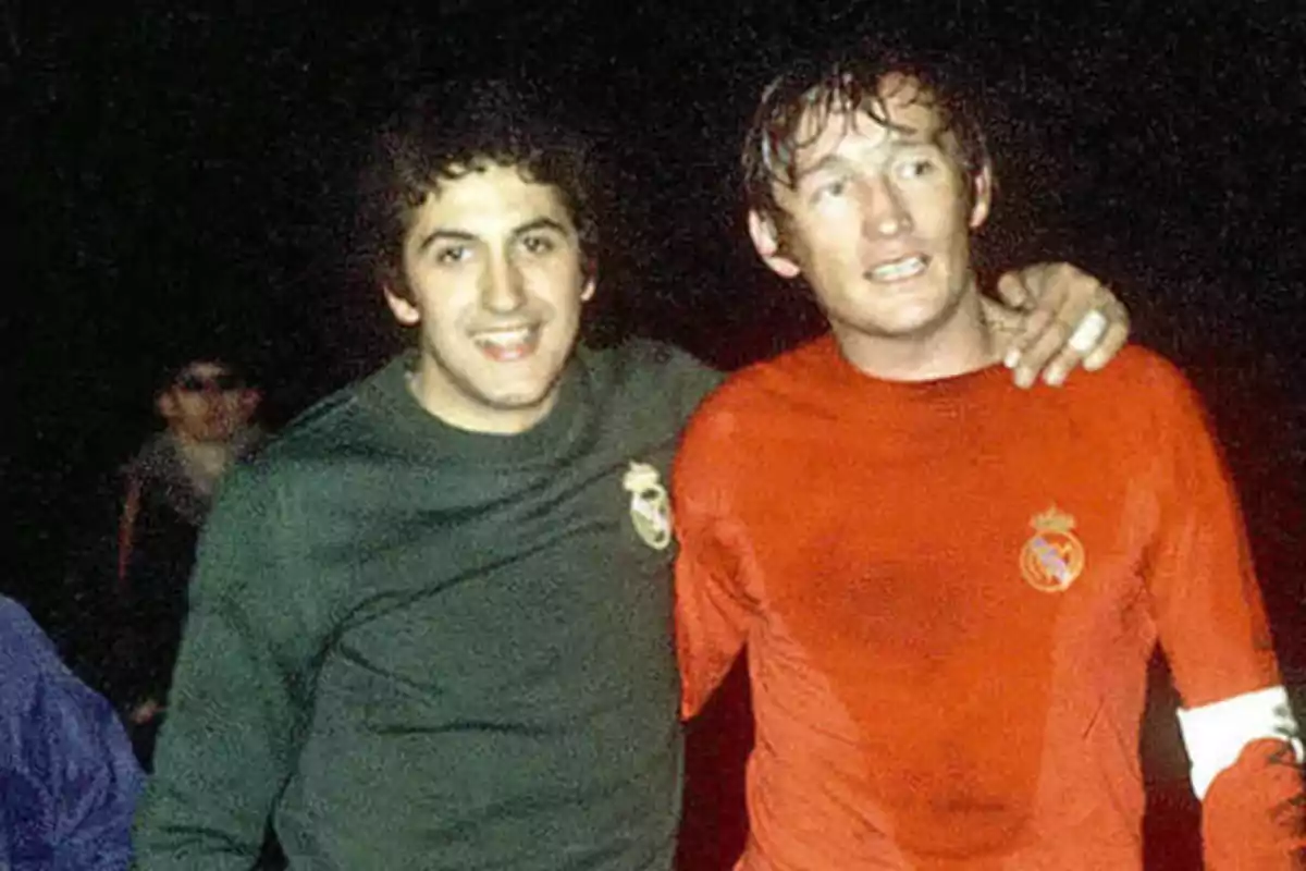 Dos jugadores de fútbol abrazados después de un partido, uno con camiseta verde y el otro con camiseta roja.