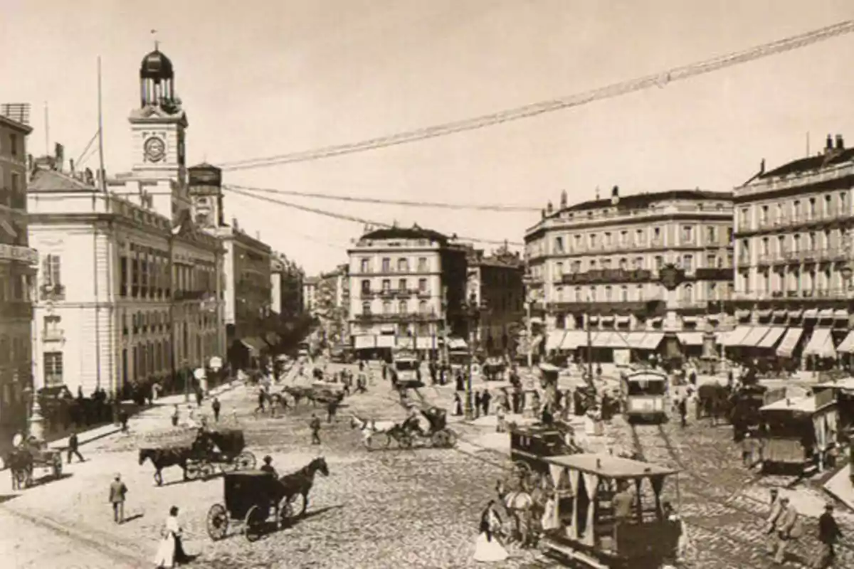 Una fotografía antigua de una plaza concurrida con edificios históricos, carruajes tirados por caballos y personas caminando.