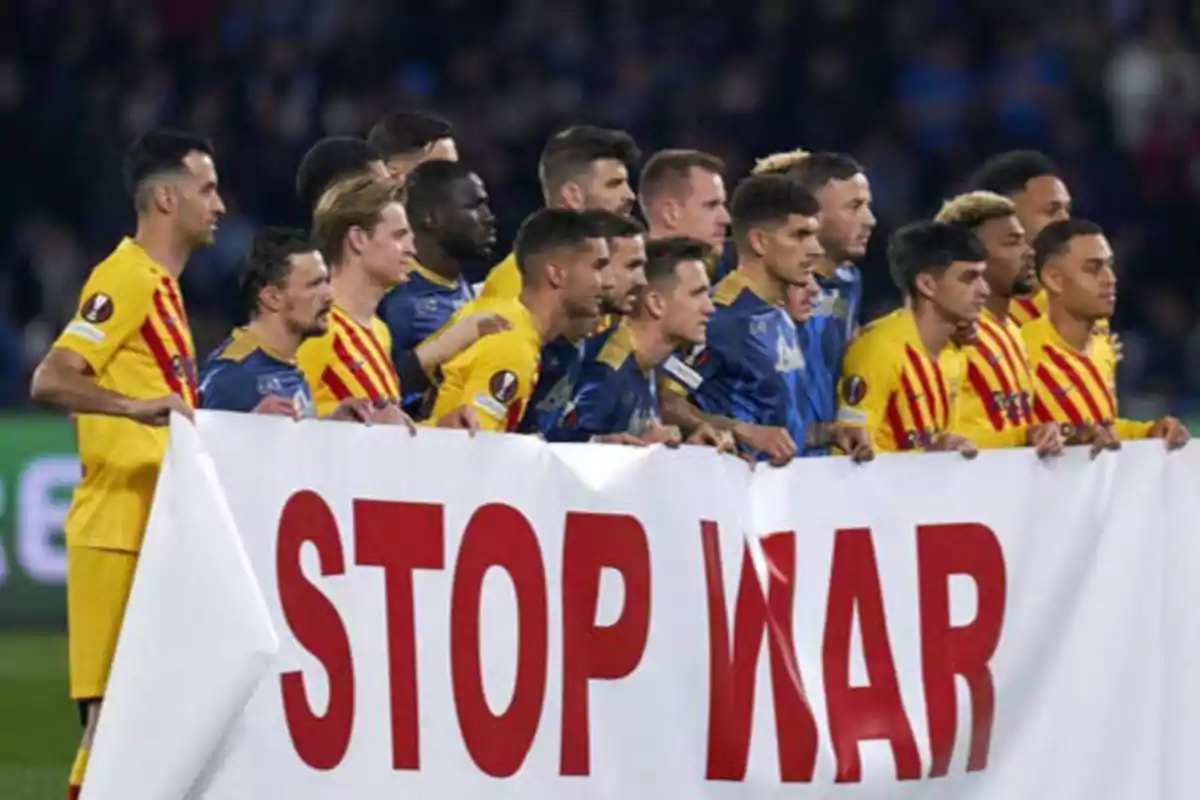 Jugadores de fútbol de dos equipos diferentes sostienen una pancarta con el mensaje "STOP WAR" antes de un partido.