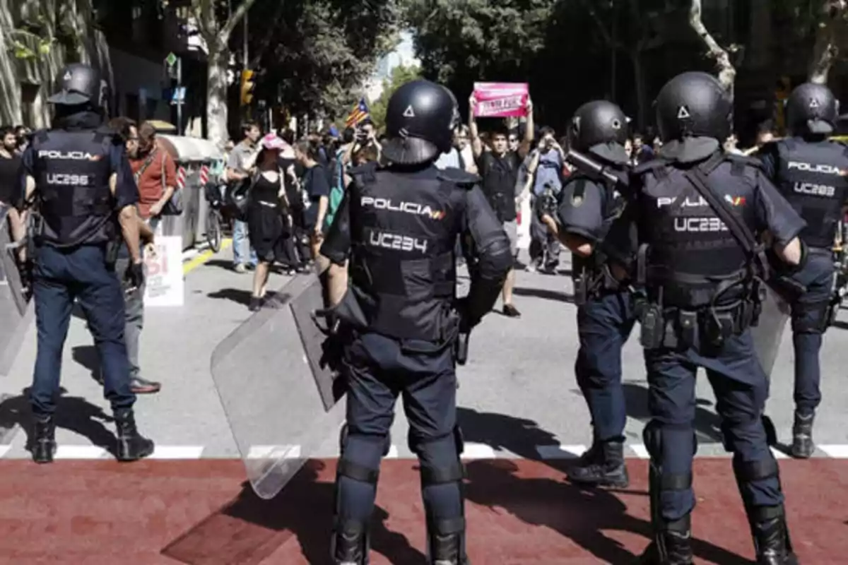 Policías antidisturbios con equipo de protección se enfrentan a una multitud de manifestantes en una calle.