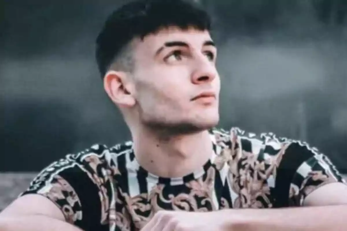 Un hombre joven con una camiseta de rayas y diseño floral, mirando hacia arriba con una expresión pensativa.