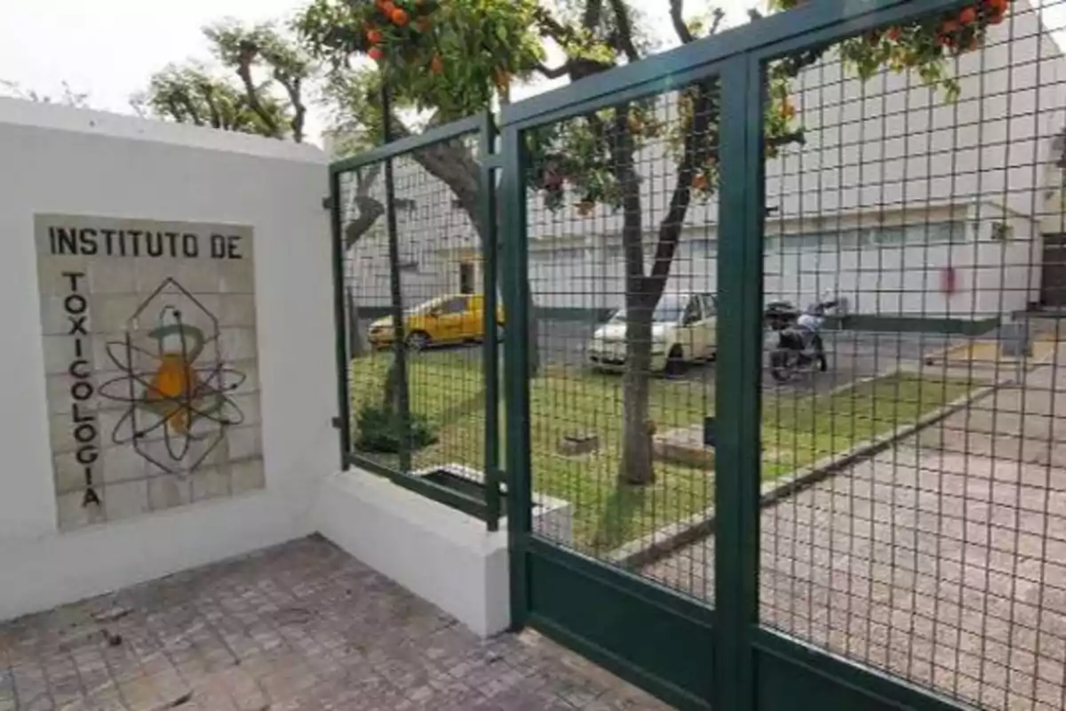 Entrada del Instituto de Toxicología con un portón de malla metálica y un letrero en la pared.