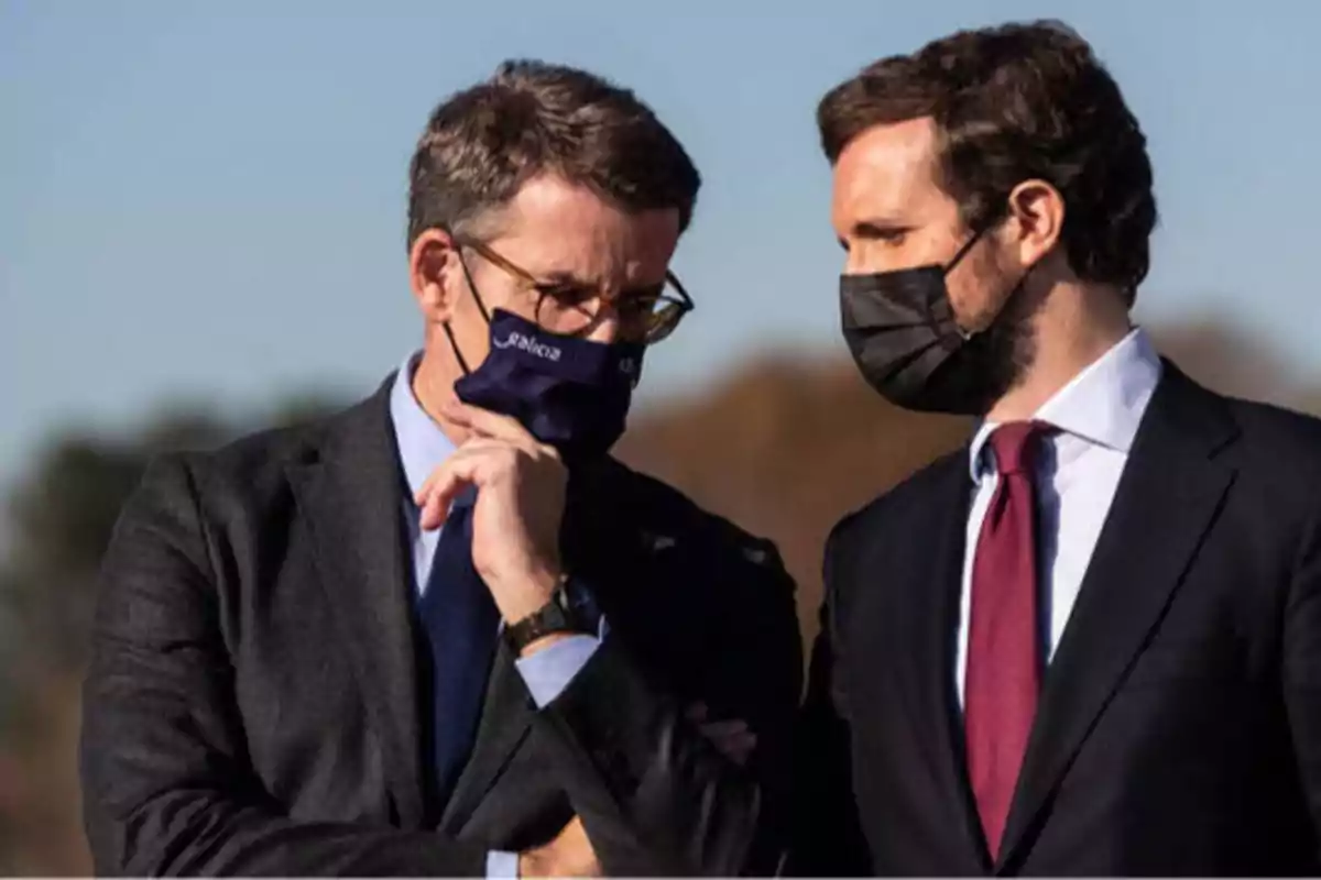 Dos hombres con mascarillas conversando al aire libre.