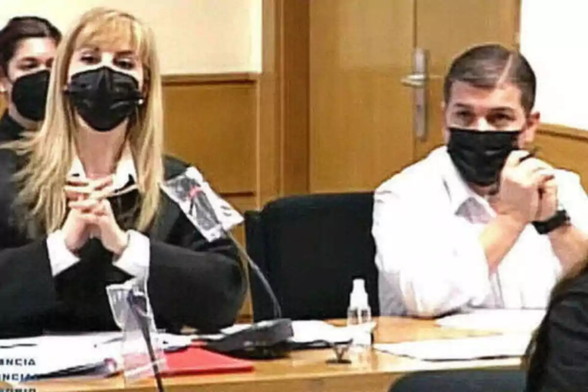 Personas con mascarillas negras sentadas en una mesa en lo que parece ser una reunión o audiencia.