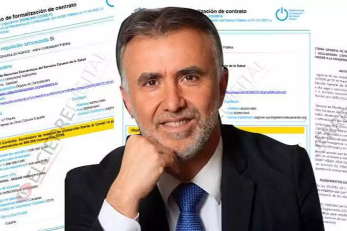 Un hombre con traje y corbata azul sonriendo, con documentos de formalización de contrato en el fondo.