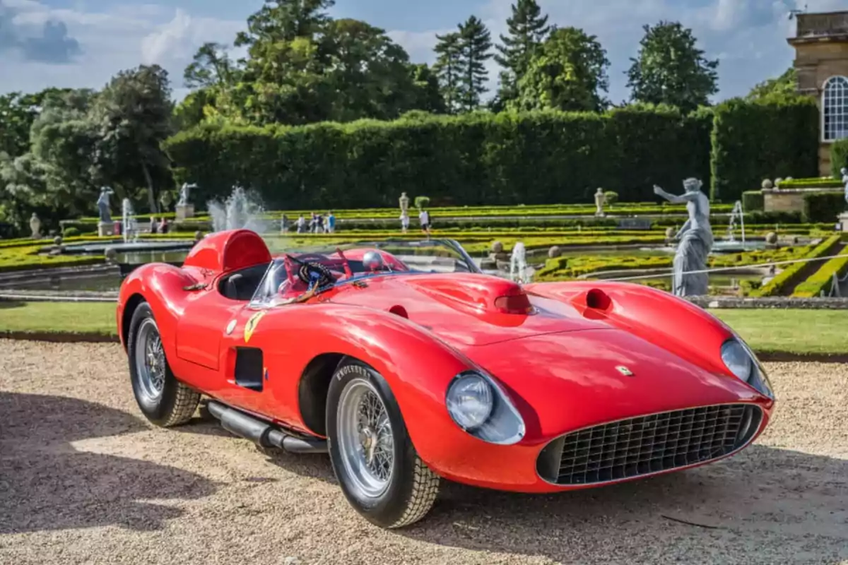 Un coche deportivo clásico Ferrari 0674 rojo estacionado en un jardín con fuentes y estatuas al fondo.