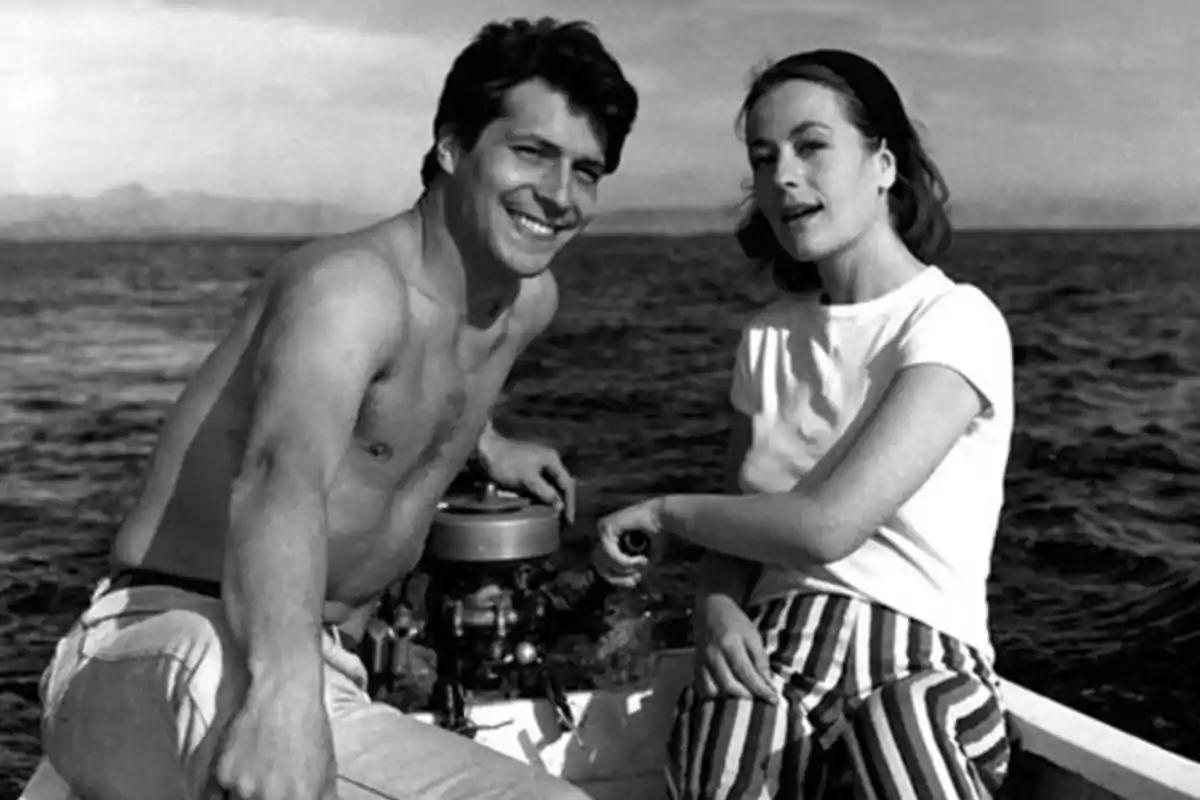 Una pareja sonriente en un bote en el mar, el hombre está sin camisa y la mujer lleva una camiseta blanca y pantalones a rayas. Una pareja sonriente en un bote en el mar, el hombre está sin camisa y la mujer lleva una camiseta blanca y pantalones a rayas.