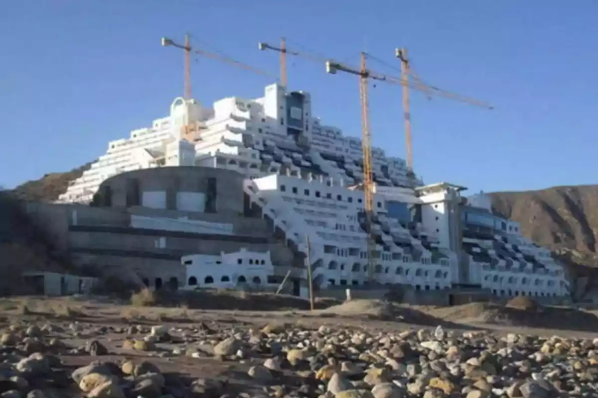 Edificio en construcción con grúas en un paisaje árido y rocoso.