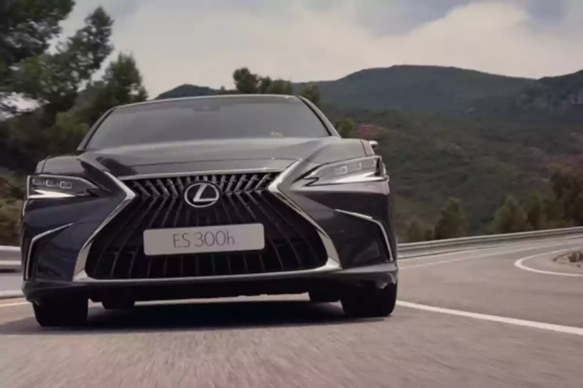 Un coche Lexus ES 300h negro conduciendo en una carretera con montañas y árboles al fondo.