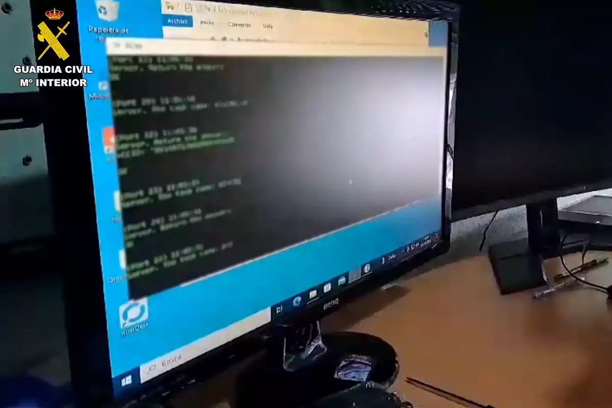 Un monitor de computadora muestra una pantalla con texto en un entorno de escritorio, mientras que en la esquina superior izquierda se observa el logotipo de la Guardia Civil y el texto 