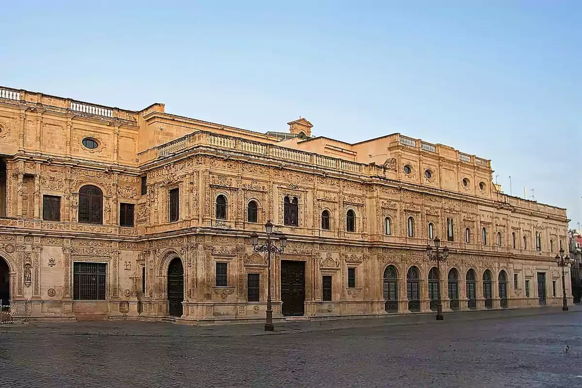Fachada de un edificio histórico de piedra con detalles ornamentales y ventanas arqueadas en una plaza vacía bajo un cielo despejado Fachada de un edificio histórico de piedra con detalles ornamentales y ventanas arqueadas en una plaza vacía bajo un cielo despejado