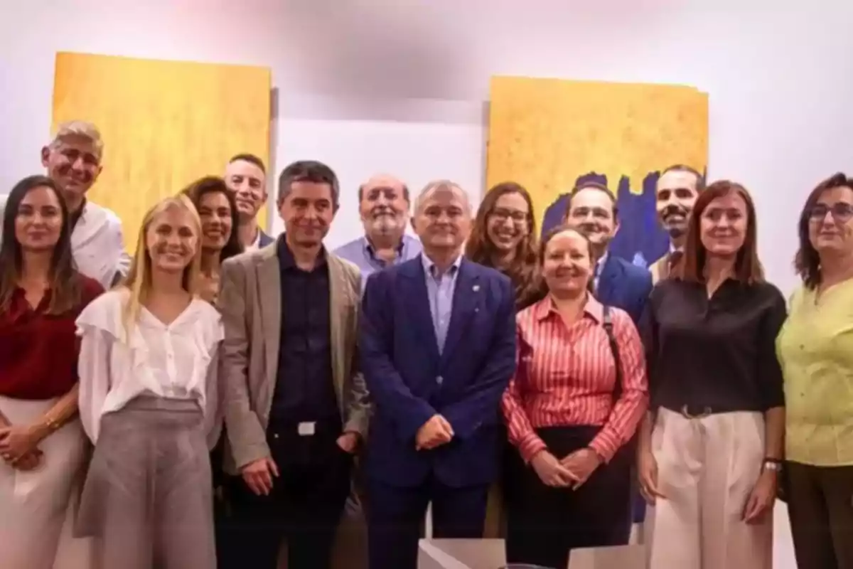 Grupo de personas posando juntas en una oficina con cuadros amarillos en la pared de fondo Grupo de personas posando juntas en una oficina con cuadros amarillos en la pared de fondo