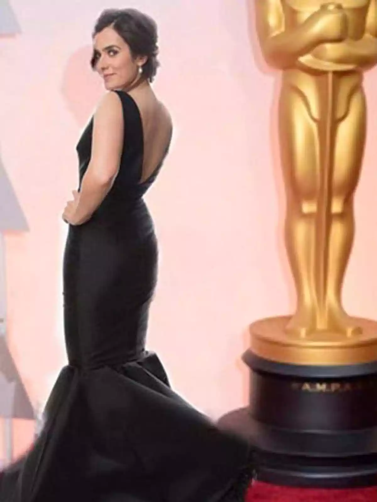 Mujer con vestido negro elegante posando en una alfombra roja junto a una gran estatua dorada de los premios Oscar Mujer con vestido negro elegante posando en una alfombra roja junto a una gran estatua dorada de los premios Oscar