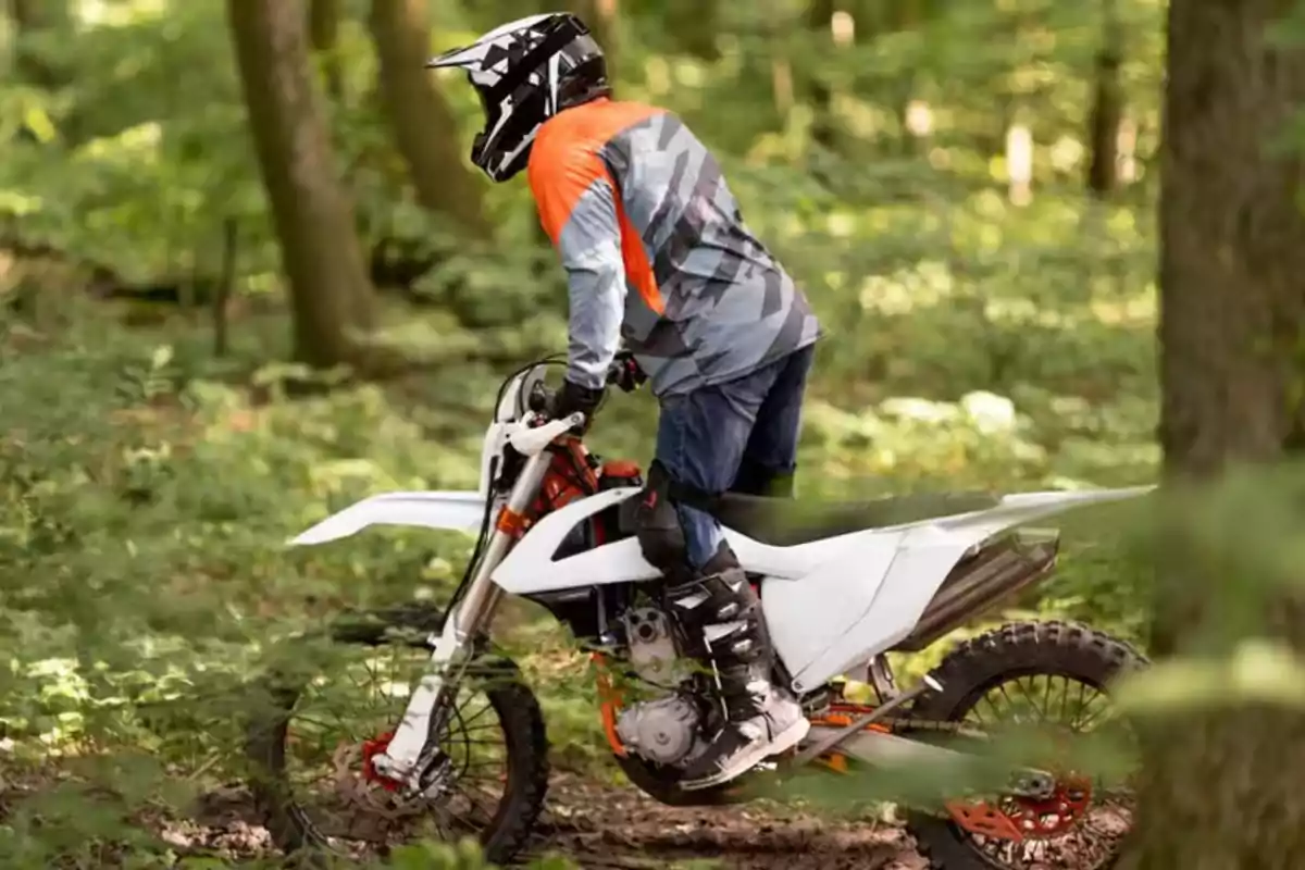 Persona con casco y ropa de protección montando una moto de cross blanca en un bosque