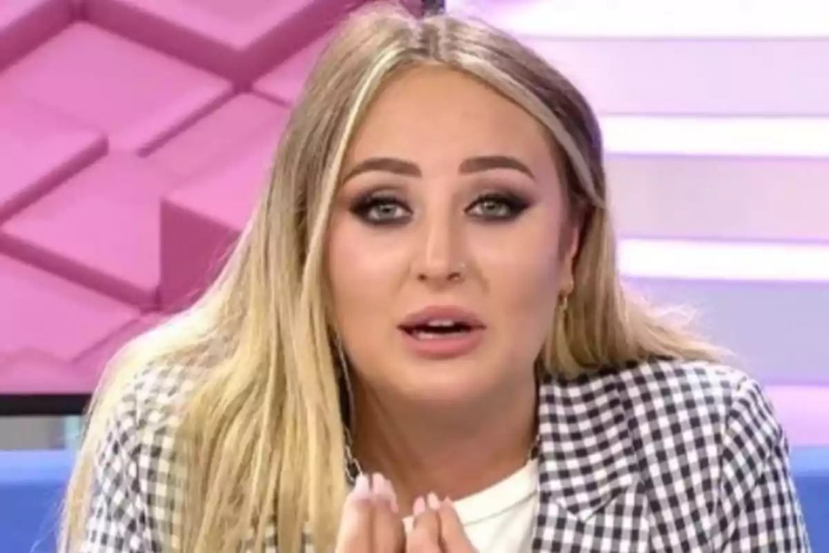 Mujer rubia con chaqueta de cuadros en un set de televisión con fondo rosa y blanco Mujer rubia con chaqueta de cuadros en un set de televisión con fondo rosa y blanco