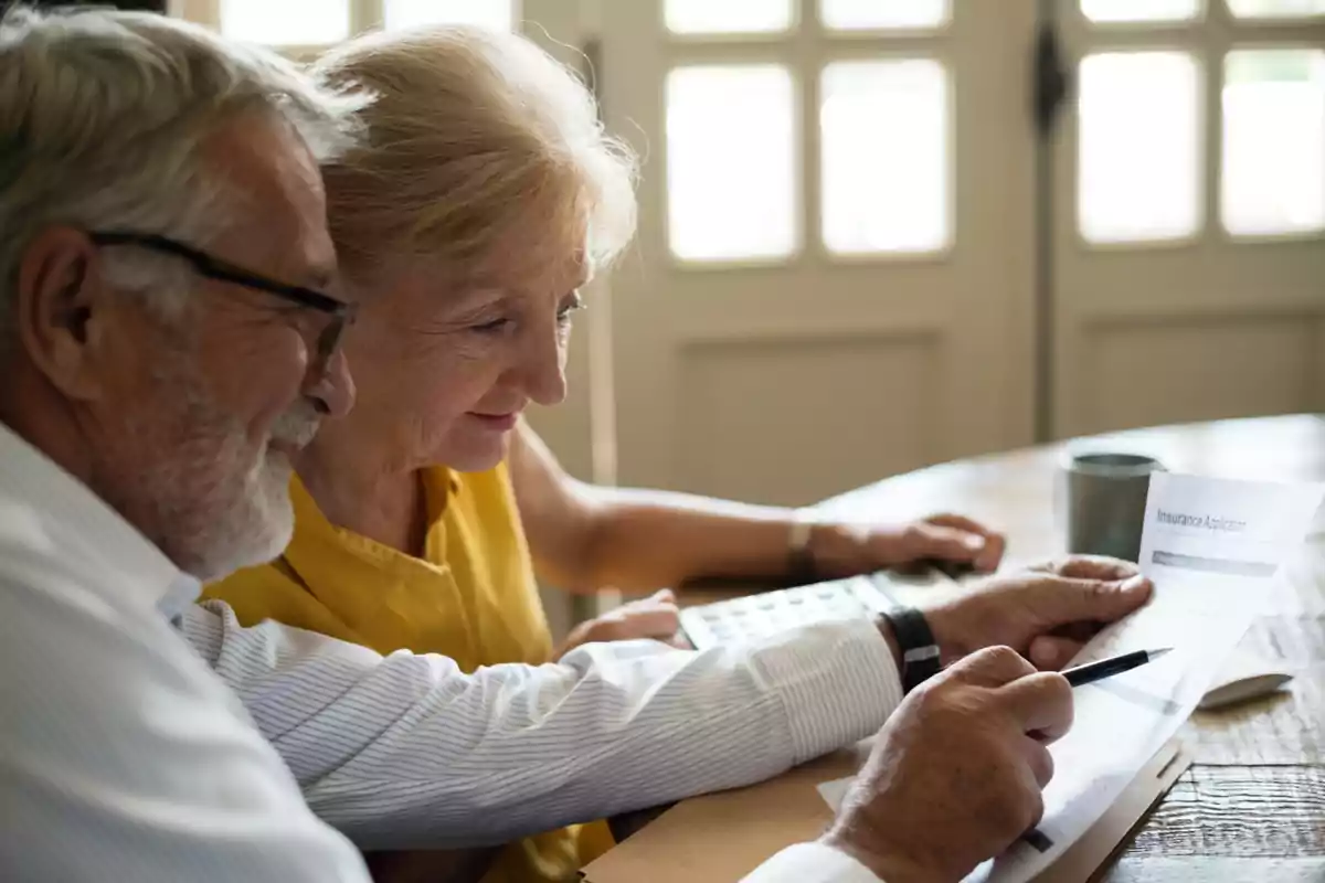 Pareja de personas mayores revisando documentos y usando una calculadora en una mesa Pareja de personas mayores revisando documentos y usando una calculadora en una mesa