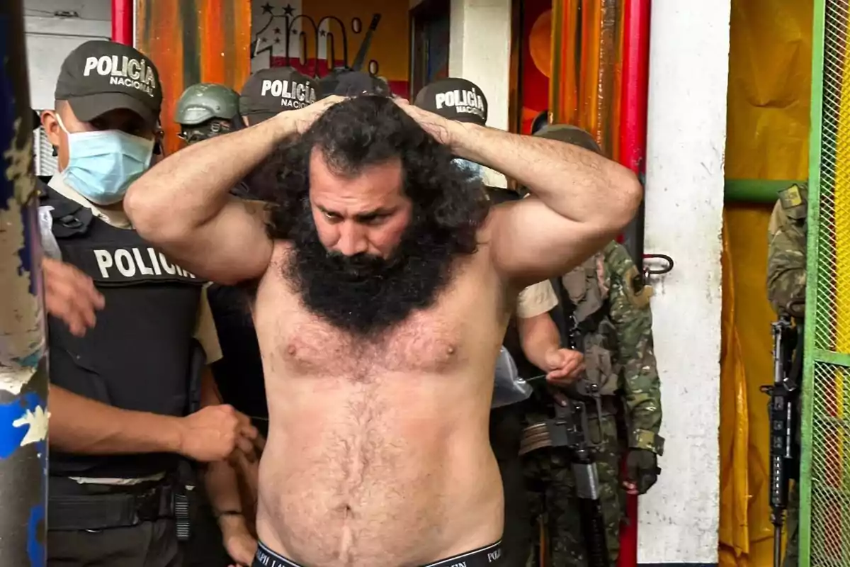 Hombre sin camisa con las manos en la cabeza escoltado por varios policías armados dentro de un edificio Hombre sin camisa con las manos en la cabeza escoltado por varios policías armados dentro de un edificio