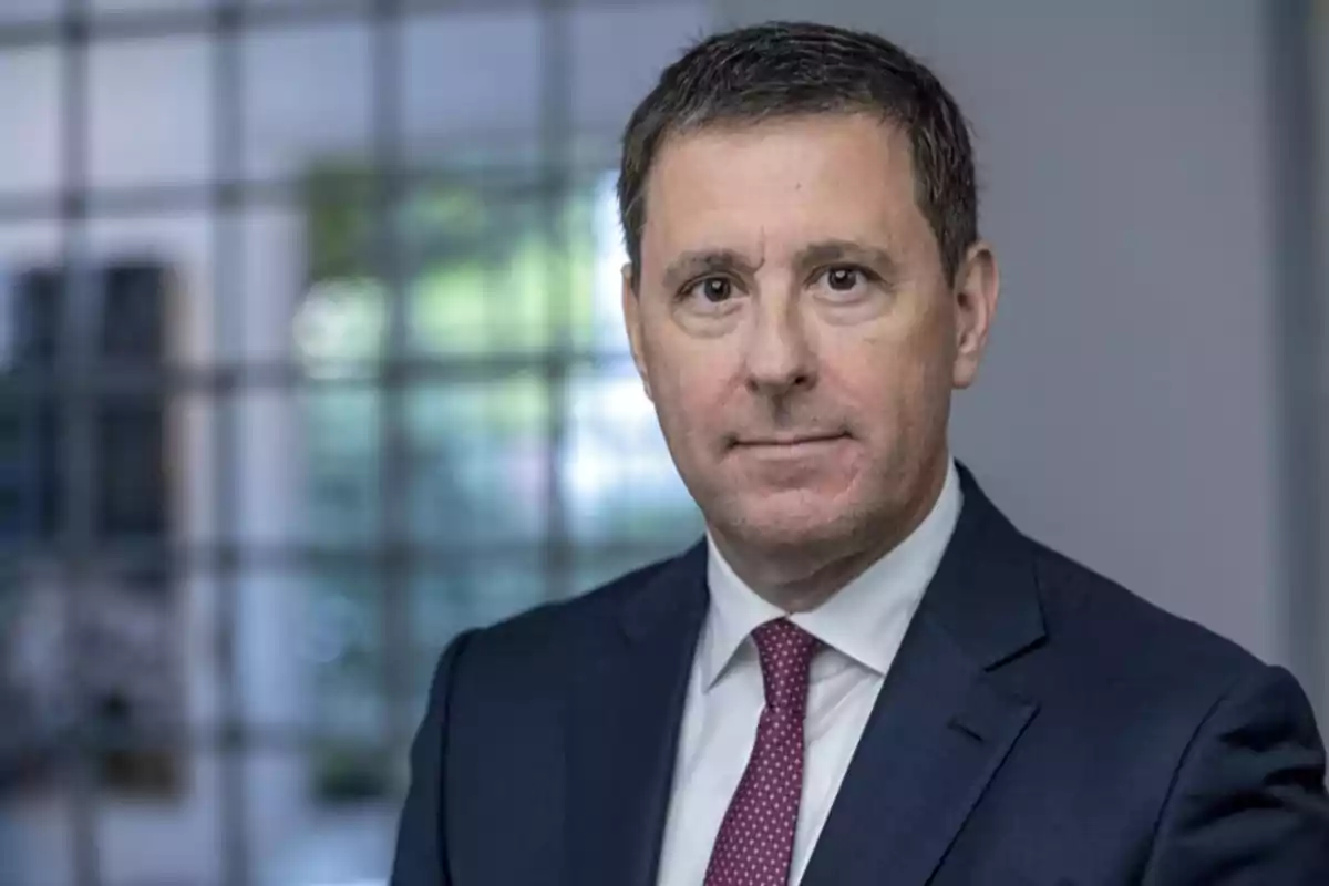 Hombre de mediana edad con cabello corto y oscuro vistiendo traje azul y corbata roja en un entorno de oficina desenfocado Hombre de mediana edad con cabello corto y oscuro vistiendo traje azul y corbata roja en un entorno de oficina desenfocado