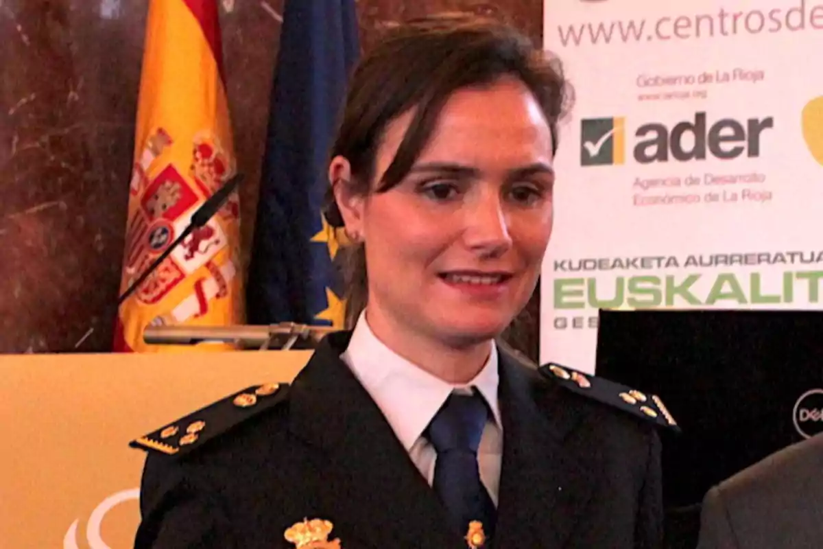 Mujer con uniforme de policía posando en un evento oficial con banderas y carteles institucionales de fondo