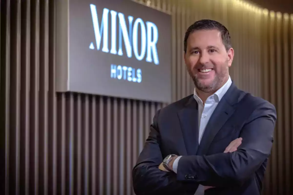Hombre de traje sonriente con los brazos cruzados frente a un letrero que dice Minor Hotels