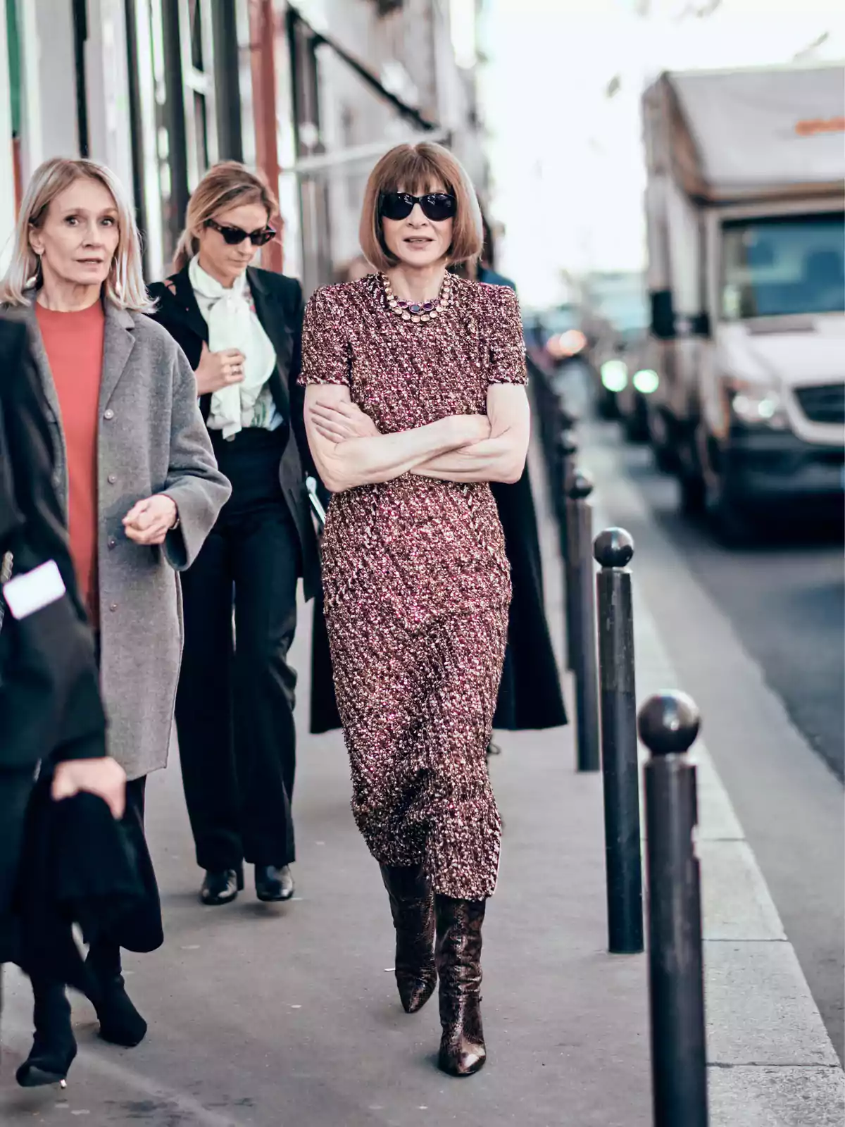 Mujer con vestido brillante y gafas de sol caminando por la calle acompañada de otras personas en un entorno urbano Mujer con vestido brillante y gafas de sol caminando por la calle acompañada de otras personas en un entorno urbano