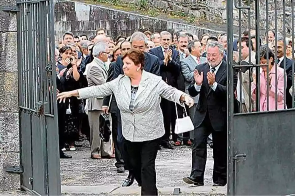 Mujer abriendo una puerta de hierro mientras una multitud aplaude detrás de ella Mujer abriendo una puerta de hierro mientras una multitud aplaude detrás de ella