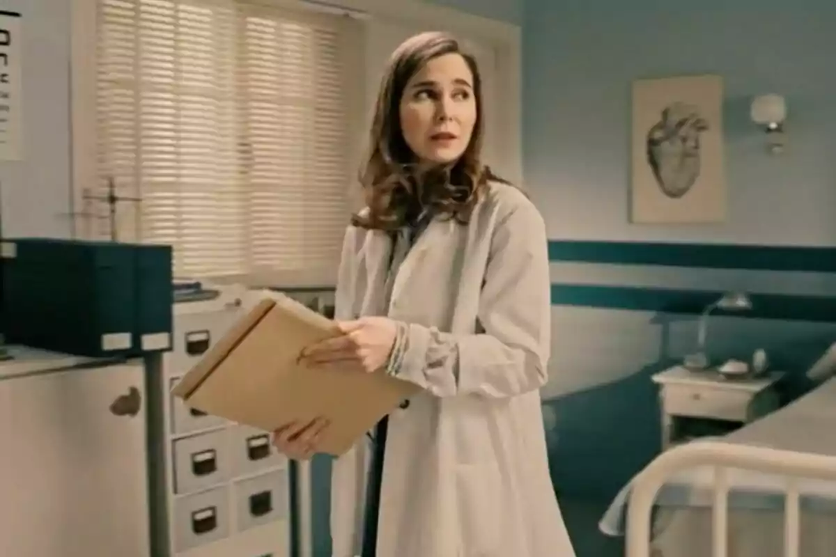 Natalia Sánchez (interpretando a Begoña en 'Sueños de Libertad') con bata de laboratorio sosteniendo una carpeta en una habitación médica con una cama y un dibujo de un corazón en la pared. Natalia Sánchez (interpretando a Begoña en 'Sueños de Libertad') con bata de laboratorio sosteniendo una carpeta en una habitación médica con una cama y un dibujo de un corazón en la pared.
