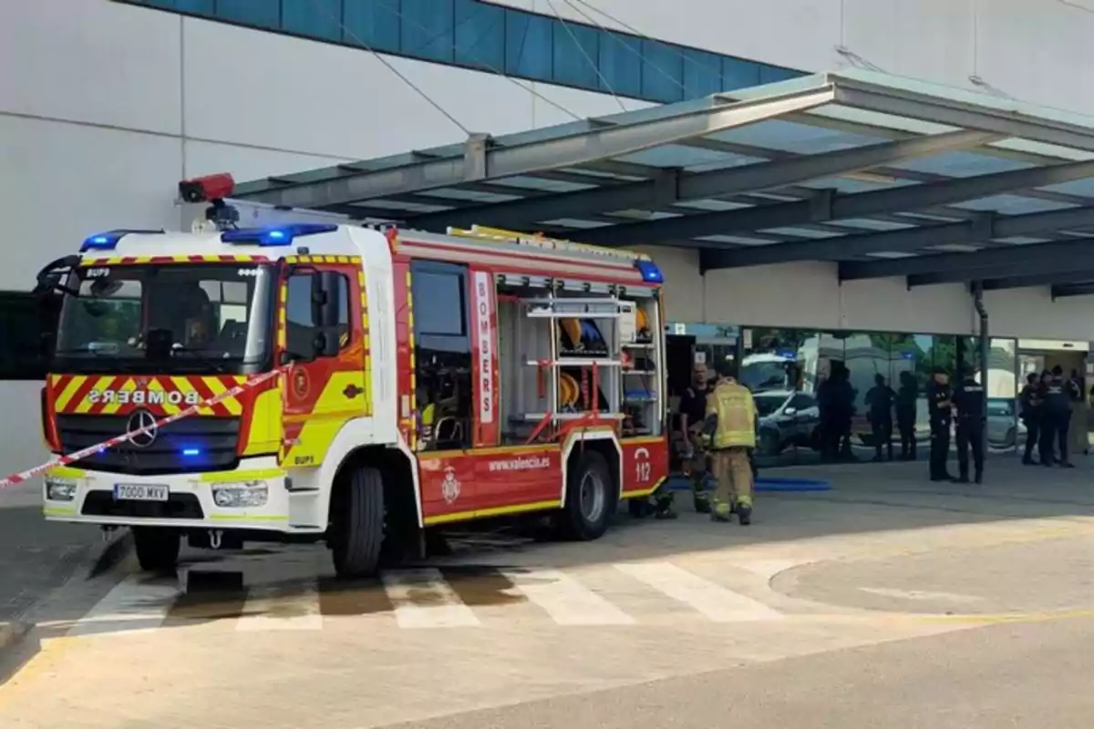 Camión de bomberos estacionado frente a la entrada de un edificio con varios bomberos y policías en la escena