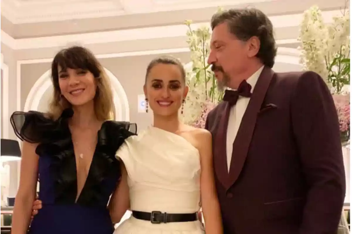 Tres personas elegantemente vestidas posan sonrientes en un evento formal con un fondo decorado con flores blancas y rosadas Tres personas elegantemente vestidas posan sonrientes en un evento formal con un fondo decorado con flores blancas y rosadas