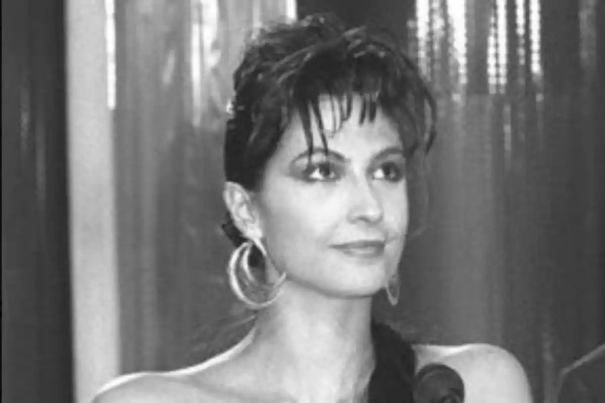 Mujer joven de cabello oscuro y corto con aretes grandes, mirando hacia el frente y sonriendo levemente, en una imagen en blanco y negro Mujer joven de cabello oscuro y corto con aretes grandes, mirando hacia el frente y sonriendo levemente, en una imagen en blanco y negro
