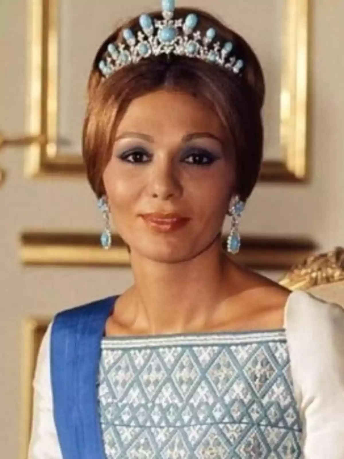 Mujer elegantemente vestida con tiara y joyas turquesa, lleva un vestido blanco con detalles azules y posa en un entorno lujoso Mujer elegantemente vestida con tiara y joyas turquesa, lleva un vestido blanco con detalles azules y posa en un entorno lujoso