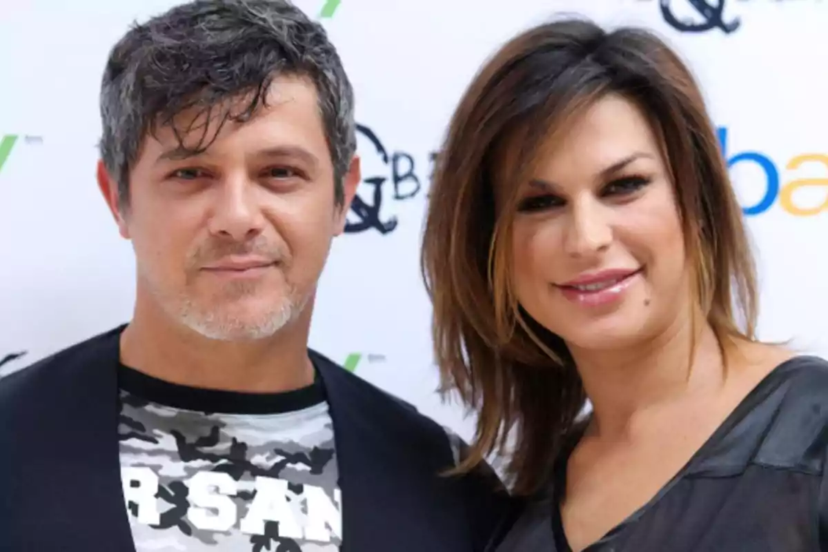 Un hombre y una mujer posan juntos y sonríen frente a un fondo con logotipos. Un hombre y una mujer posan juntos y sonríen frente a un fondo con logotipos.