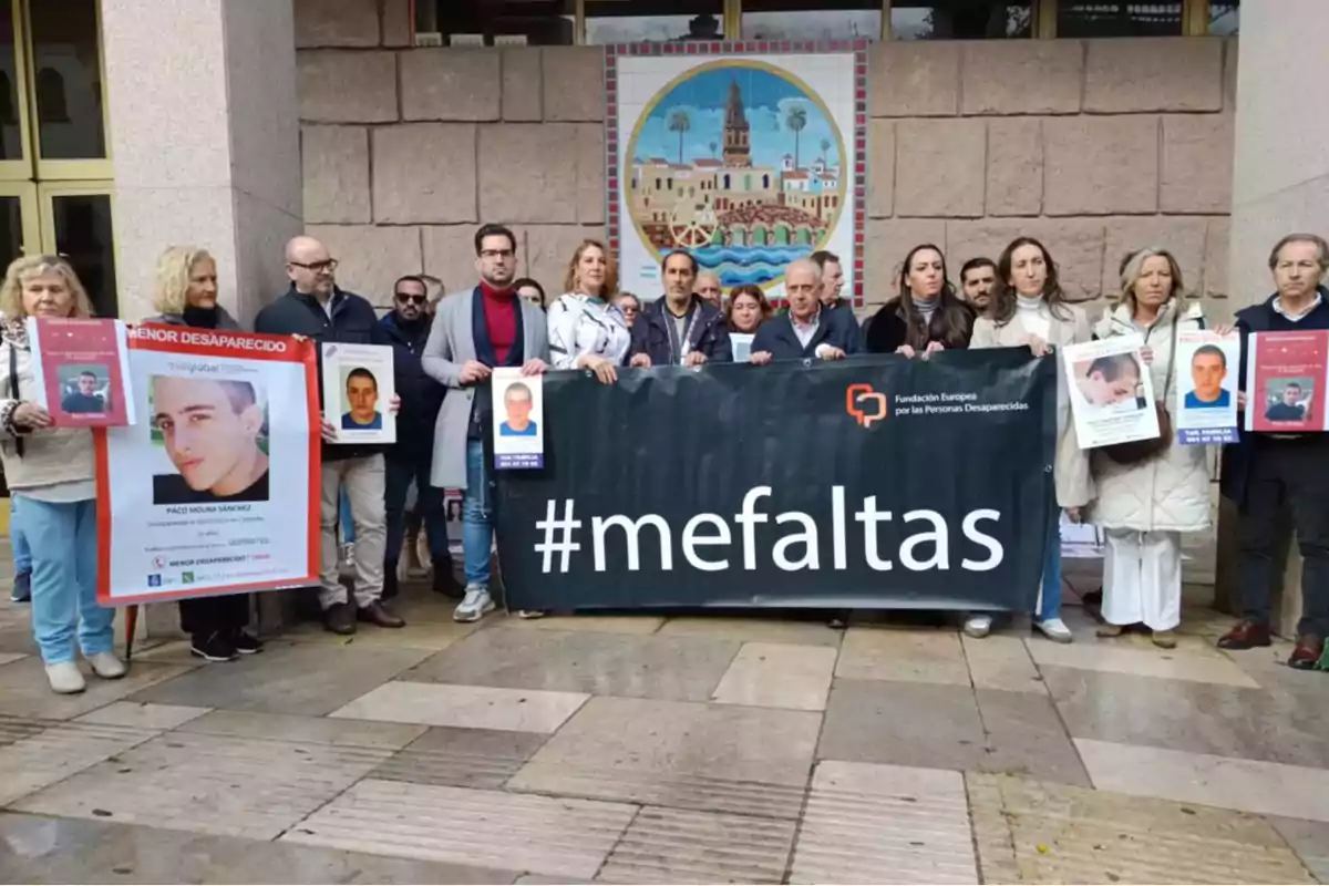 Grupo de personas sosteniendo pancartas y fotografías de personas desaparecidas junto a una lona negra con el hashtag mefaltas frente a un edificio con un mural colorido al fondo Grupo de personas sosteniendo pancartas y fotografías de personas desaparecidas junto a una lona negra con el hashtag mefaltas frente a un edificio con un mural colorido al fondo