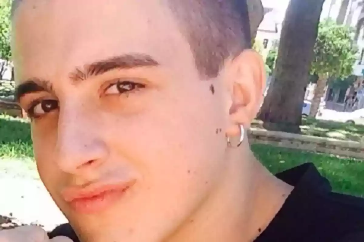 Joven con pendiente plateado en la oreja posando al aire libre en un parque Joven con pendiente plateado en la oreja posando al aire libre en un parque