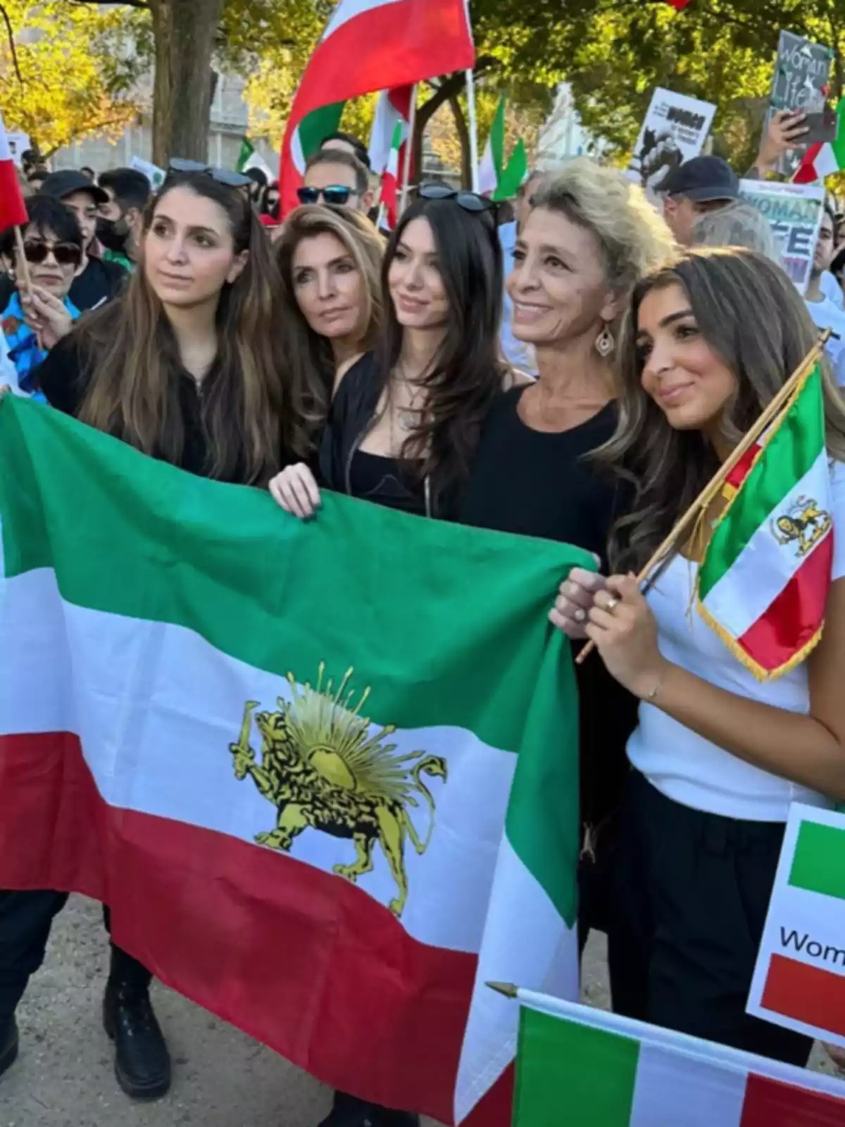 Cinco mujeres posan juntas sosteniendo una bandera de Irán con el símbolo del león y el sol durante una manifestación rodeadas de más personas y pancartas Cinco mujeres posan juntas sosteniendo una bandera de Irán con el símbolo del león y el sol durante una manifestación rodeadas de más personas y pancartas