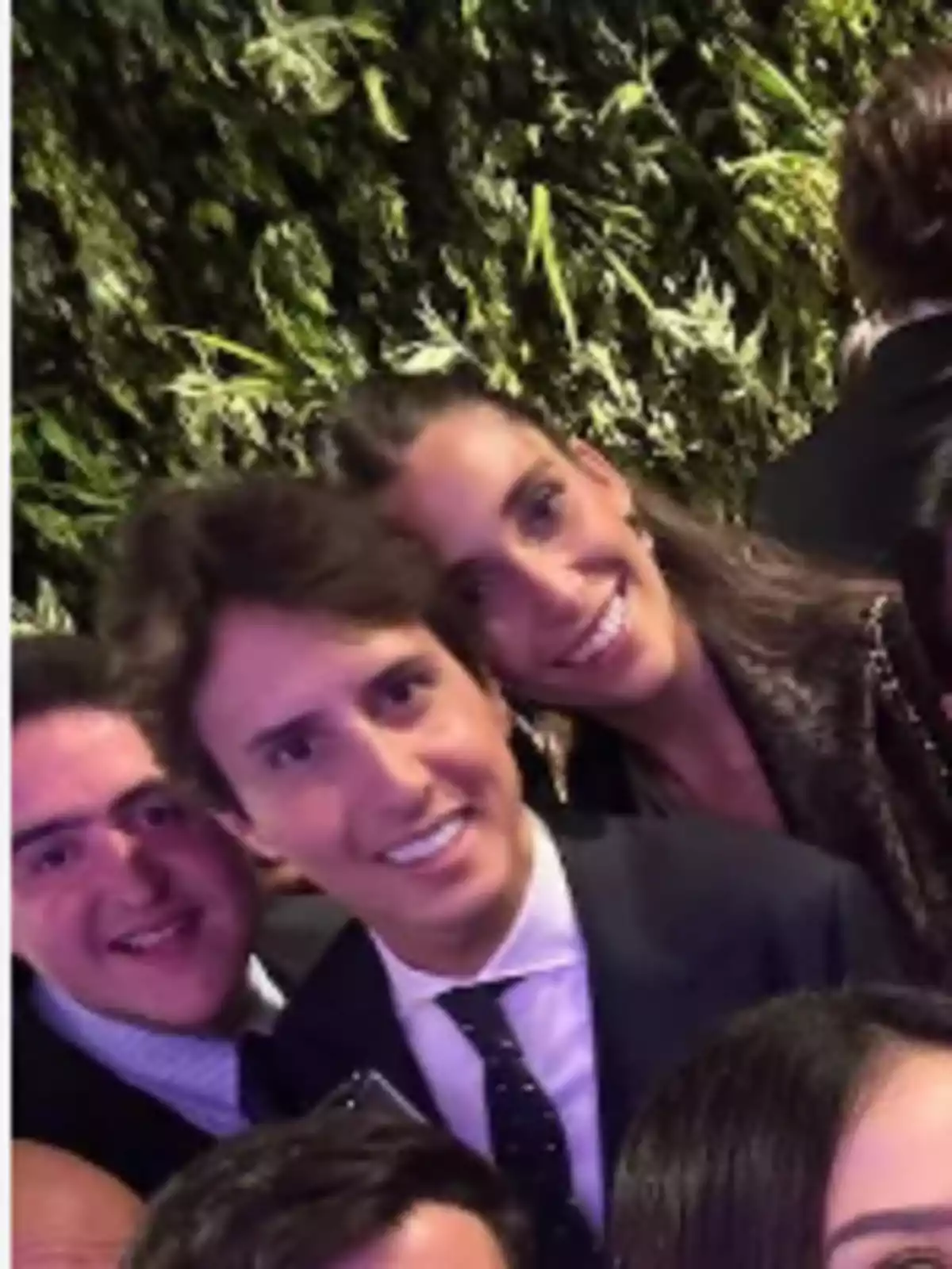 Grupo de personas jóvenes sonriendo y posando para una selfie en un evento social con fondo de plantas verdes Grupo de personas jóvenes sonriendo y posando para una selfie en un evento social con fondo de plantas verdes