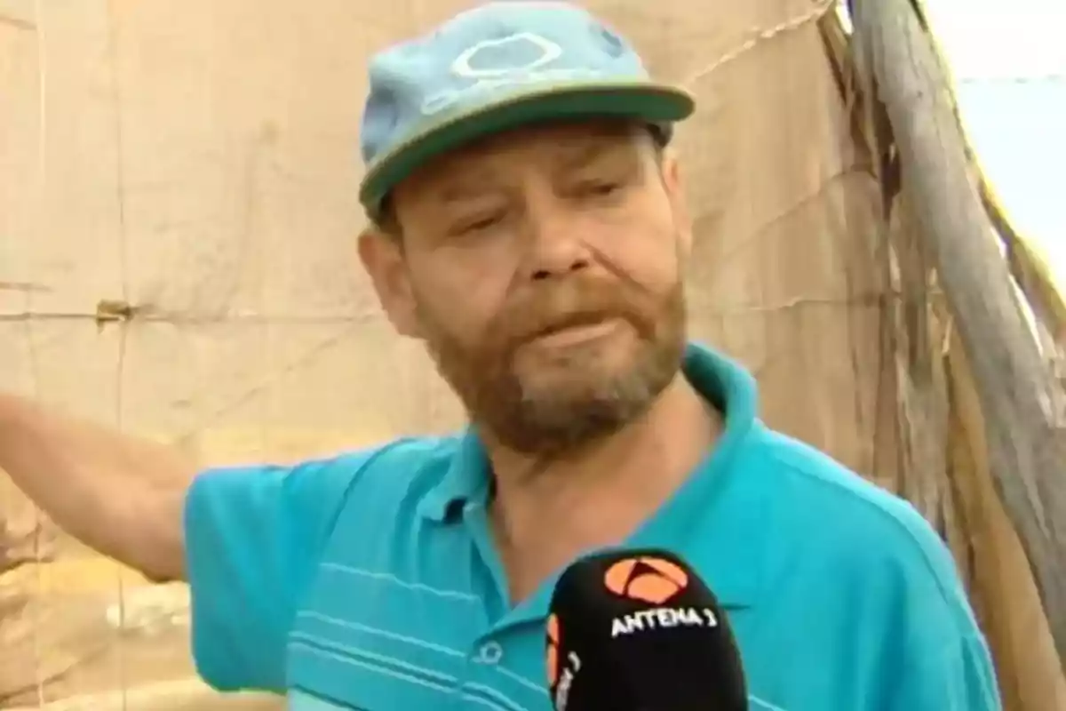 Hombre con barba y gorra azul siendo entrevistado por un canal de televisión mientras sostiene una malla