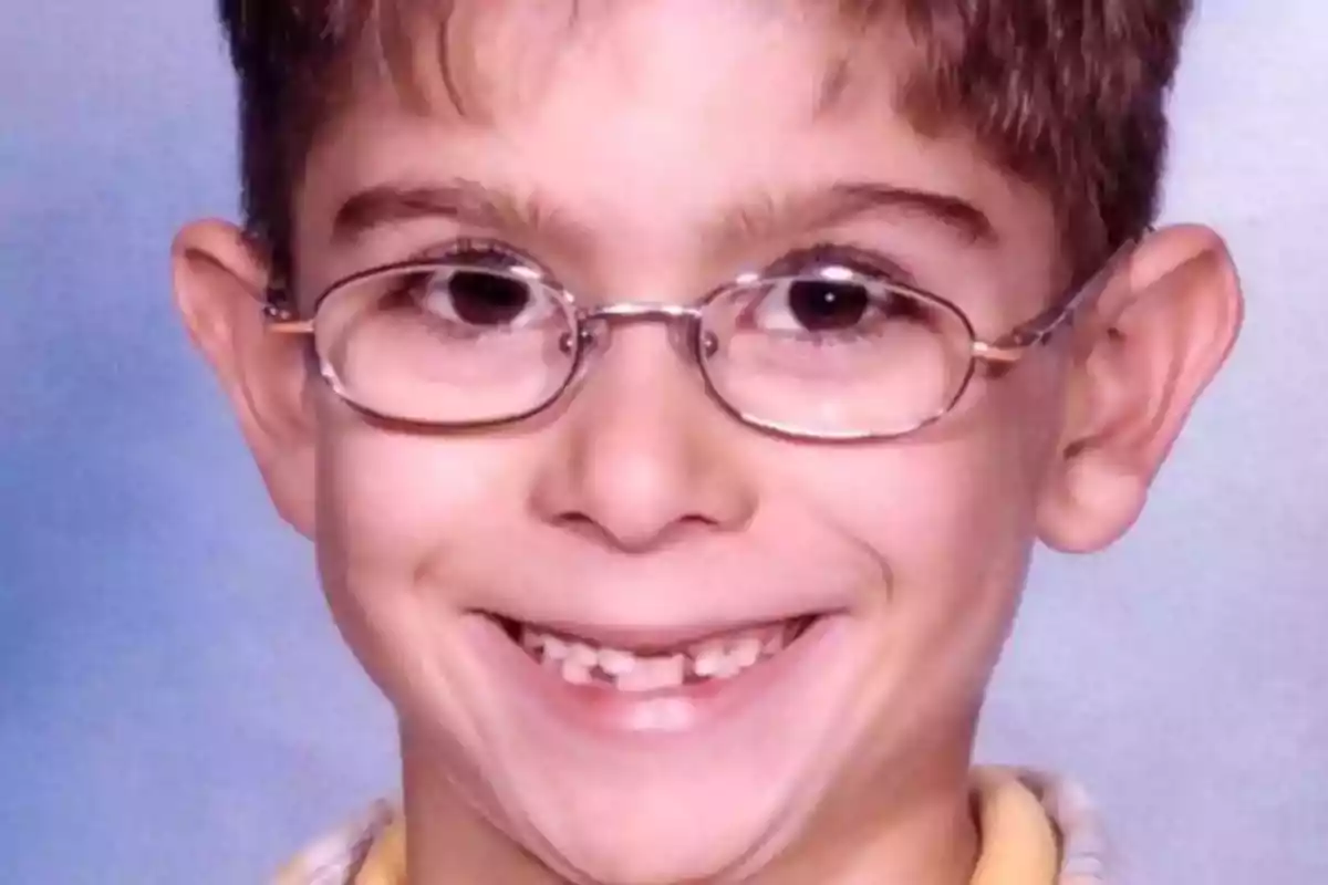 Niño con gafas sonriendo y mostrando dientes de leche con un fondo azul claro