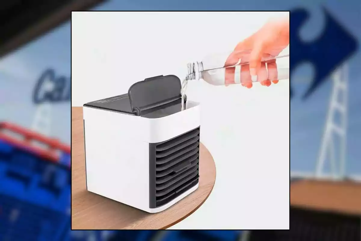 Una mano vierte agua en un mini enfriador de aire portátil blanco y negro que está sobre una mesa de madera Una mano vierte agua en un mini enfriador de aire portátil blanco y negro que está sobre una mesa de madera