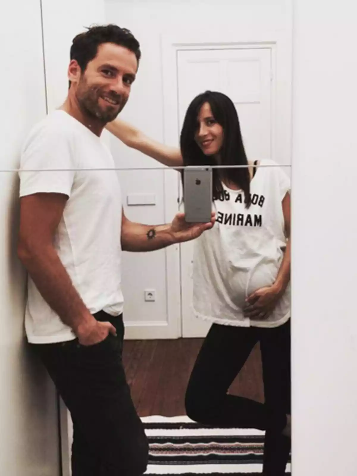 Pareja tomándose una selfie frente a un espejo, la mujer está embarazada y ambos sonríen Pareja tomándose una selfie frente a un espejo, la mujer está embarazada y ambos sonríen