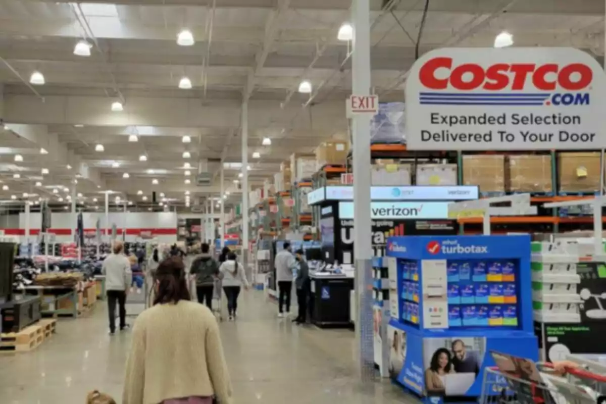 Personas caminando dentro de una tienda Costco con estantes altos llenos de productos y letreros de diferentes marcas Personas caminando dentro de una tienda Costco con estantes altos llenos de productos y letreros de diferentes marcas