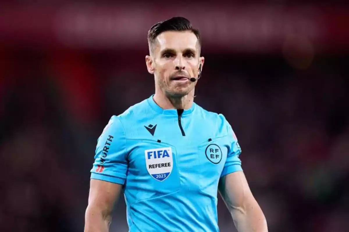Árbitro de fútbol vistiendo uniforme azul claro con insignias de FIFA y RFEF en un estadio Árbitro de fútbol vistiendo uniforme azul claro con insignias de FIFA y RFEF en un estadio